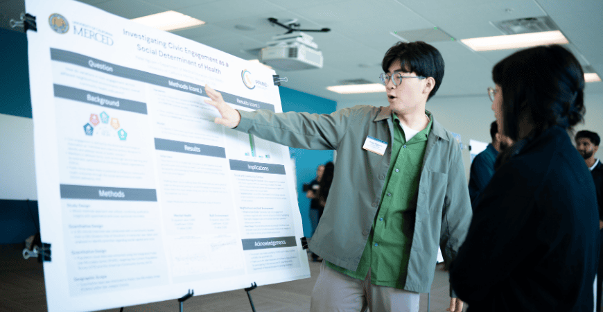 Student researcher discussing his research poster with attendee