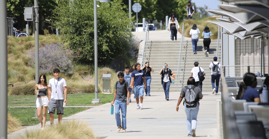 Students walk along a path in front of a staircase near The Pavilion on a sunny day at UC Merced.