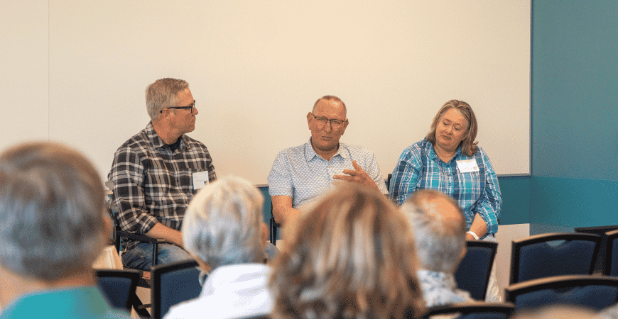 A three-person panel seated at the front of a room in front of an audience