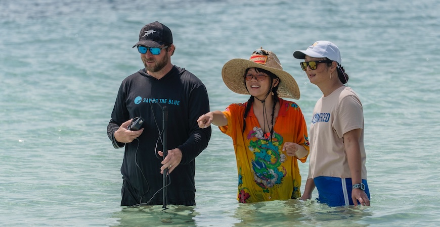 A Discovery crew member, Rei Ami and Professor Sora Kim wade through ocean water, looking ahead.