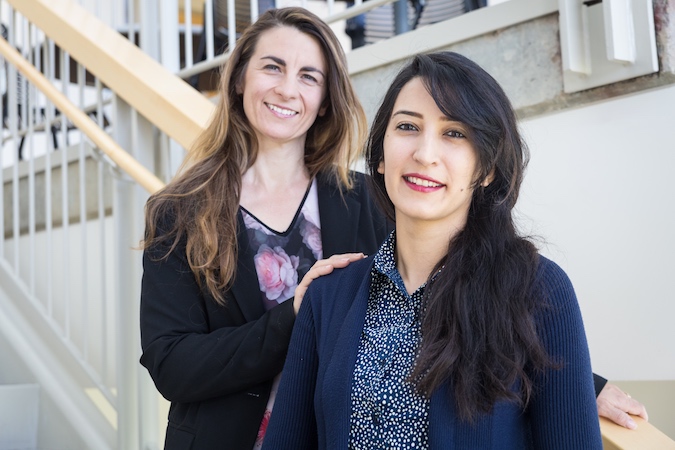 Two women pose on a stairway facing the camera.