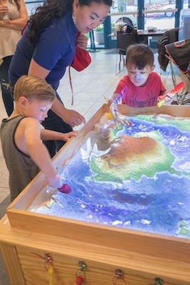 Two children and a woman at the augmented-reality sandbox.